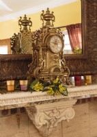 Flanquée de votives aux couleurs de bijoux, une horloge italienne antique en laiton unique en son genre préside la cheminée en pierre sculptée.
